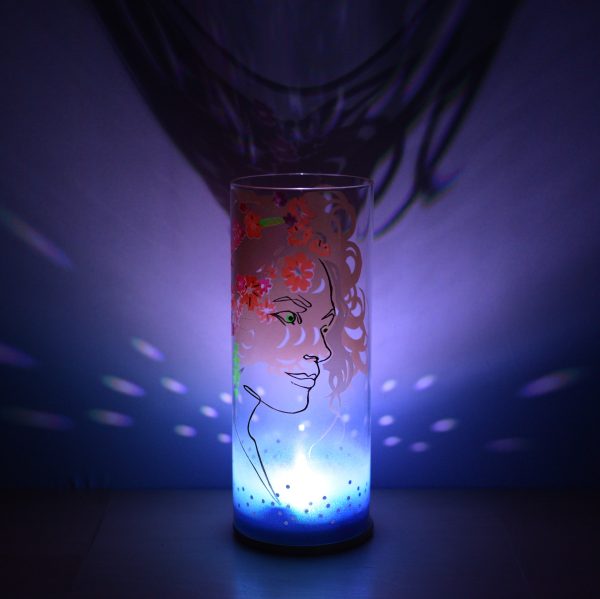 Shown on a display shelf with its LED illuminated, lamp displays brilliant patterns of light and shadow onto backdrop.