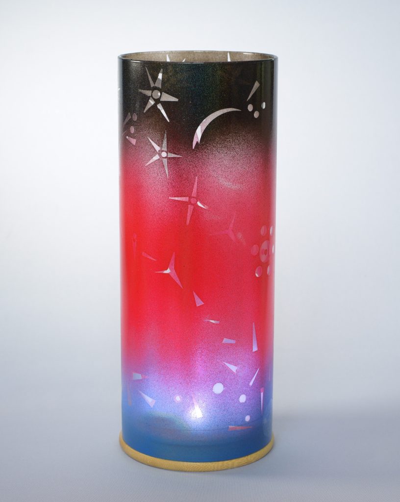 Art glass lamp shown against flood lit backdrop displaying face view.