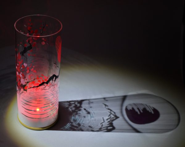 Shown under spot light at upper left, lamp displays brilliant projected shadow patterns. Highlighted are displays of patterns through the glass cylinder. LED set to color red.