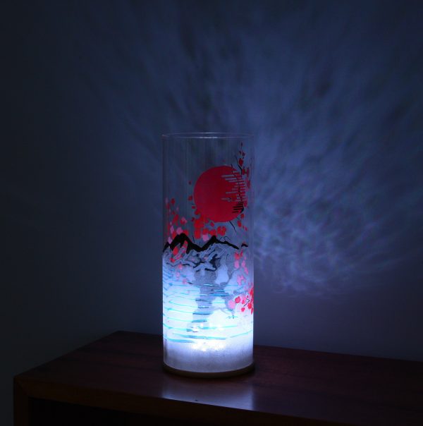 Shown on a display shelf with LED on. Unique art glass lamp displays brilliant patterns of light and shadow onto backdrop.