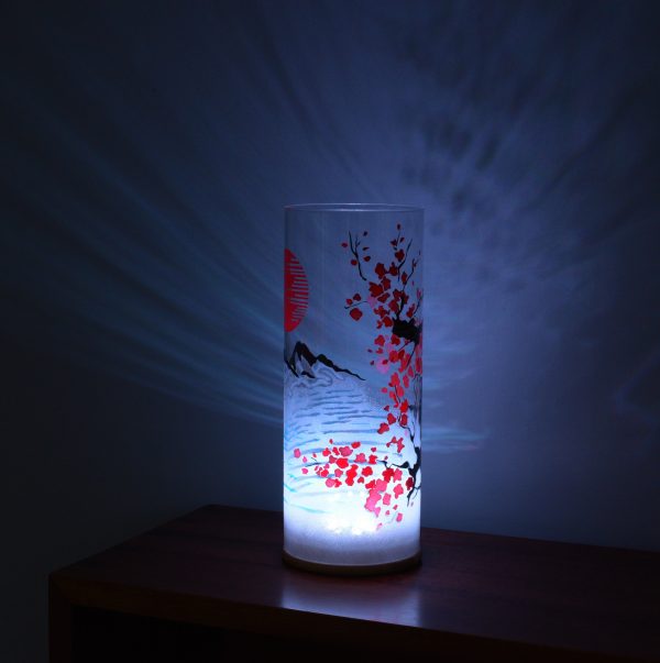 Shown on a display shelf with LED on. Unique art glass lamp displays brilliant patterns of light and shadow onto backdrop.