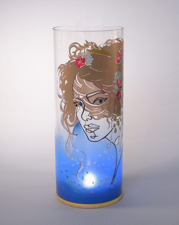 Unique art glass lamp shown against flood lit backdrop displaying face view.