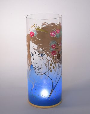 Unique art glass lamp shown against flood lit backdrop displaying face view.