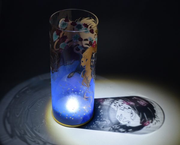 Shown under spot light at upper left, lamp displays brilliant projected shadow pattern of Athena with flowers in color. Highlighted also are displays of patterns through clear glass.