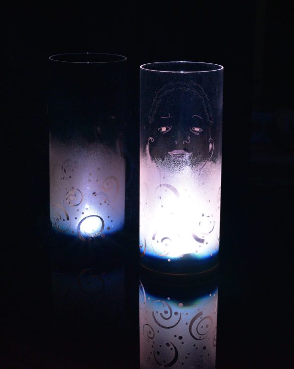 Unique art glass lamp shown placed on, and beside reflective black plexiglass while lit only by its internal LED. Lamp displays duel brilliant mirrored images.