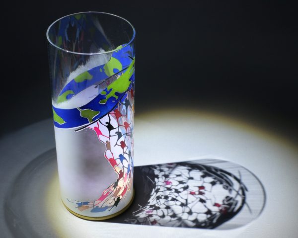 Anje Rozan shown under spot light at upper left, lamp displays brilliant projected shadow pattern. Highlighted also are displays of patterns seen through the glass cylinder.