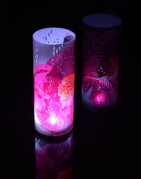 Art glass lamp shown placed on, and beside reflective black plexiglass. Lit only by its internal LED. Lamp displays duel brilliant mirrored images.