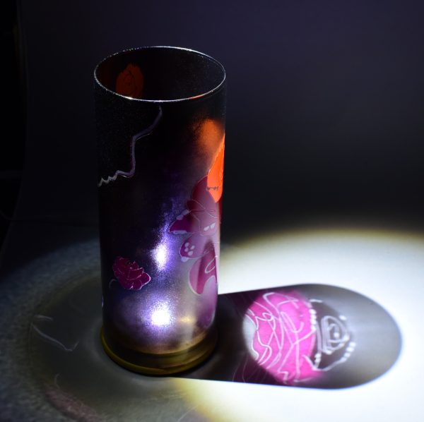 Shown under spot light at upper left, lamp displays brilliant projected image of rose and displays of patterns through clear glass. cylinder.