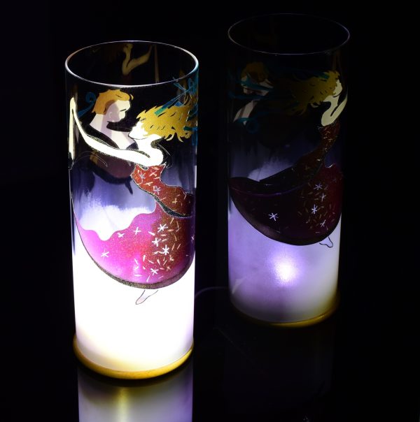 Art glass lamp shown placed on, and beside reflective black plexiglass. Lit only spot light and LED. Lamp displays duel brilliant mirrored images.