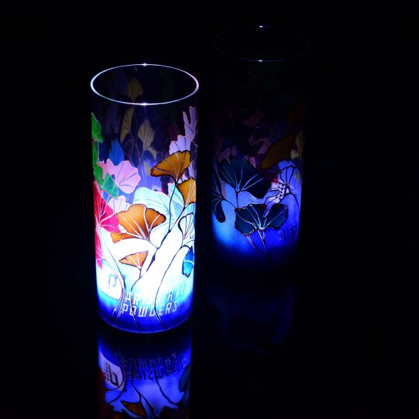 Art glass lamp shown placed on, and beside reflective black plexiglass. Lit only by its internal LED. Lamp displays duel brilliant mirrored images.